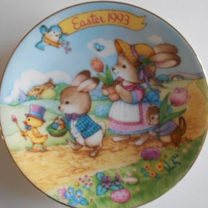 May include: A porcelain plate with a gold rim features a colorful illustration of bunnies, a chick, and a squirrel. The plate has the text "Easter 1993" on a banner.
