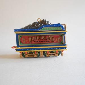 May include: A blue and yellow toy train engine ornament with a black coal car and the words "Wonderland Express" on the side. The ornament is dated 1997.