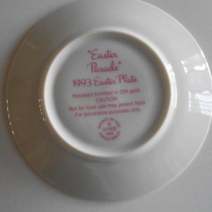 May include: White porcelain plate with a pink rim and pink text that reads "Easter Parade 1993 Easter Plate". The text continues with "Porcelain trimmed in 22K gold. CAUTION Not for food use - may poison food. For decorative purposes only." The plate also has a small pink circle with the text "Avon Collectors 1993" in white.