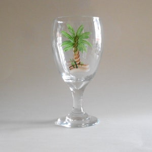 May include: A clear glass wine goblet with a hand-painted green palm tree design.
