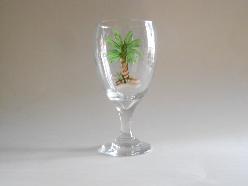 May include: A clear glass wine goblet with a hand-painted green palm tree design.