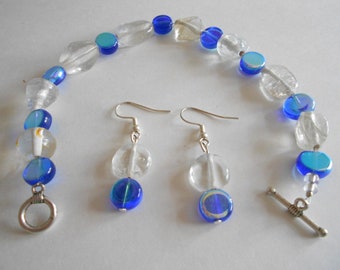 May include: A blue and clear glass beaded bracelet with a silver toggle clasp and matching blue and clear glass drop earrings with silver hooks.