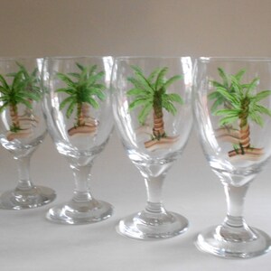 May include: Set of four clear glass wine glasses with hand-painted palm trees on each glass.