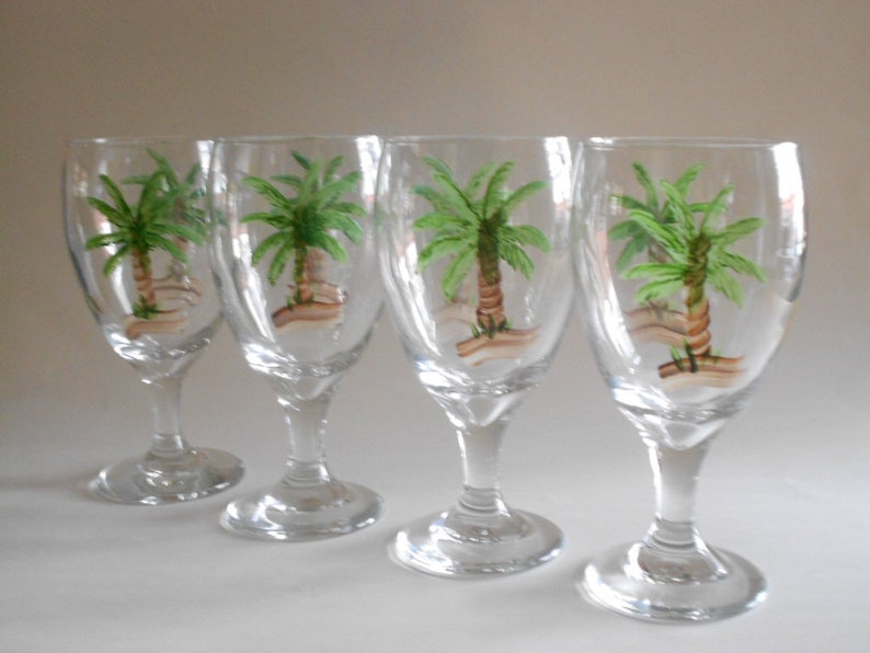 May include: Set of four clear glass wine glasses with hand-painted palm trees on each glass.