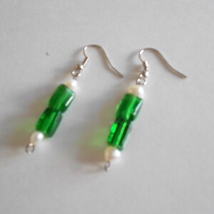 Pu&ograve; includere: Un paio di orecchini verdi e bianchi con un gancio d'argento. Gli orecchini sono realizzati con perline di vetro verde e perline di perla bianca.
