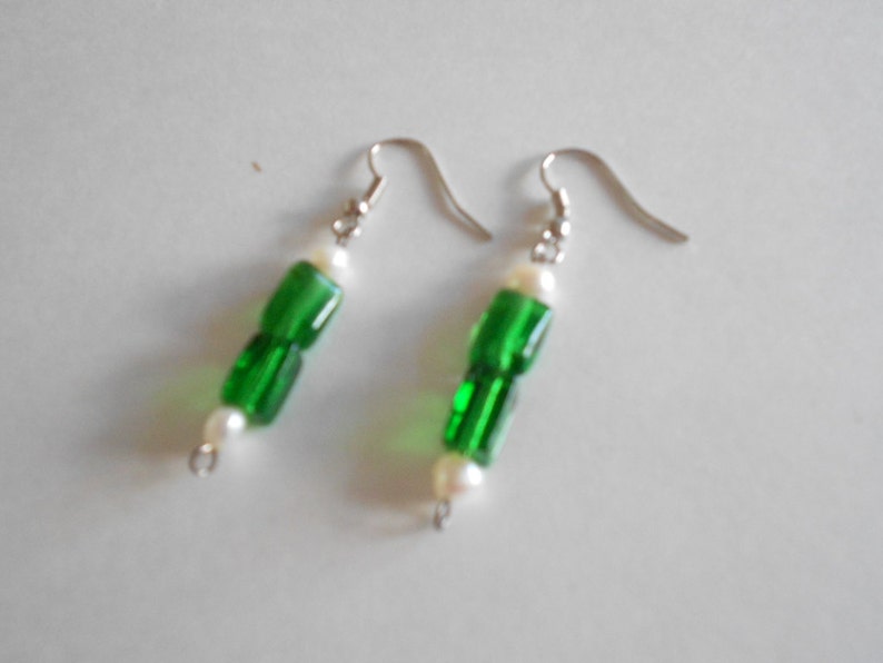 Pu&ograve; includere: Un paio di orecchini verdi e bianchi con un gancio d'argento. Gli orecchini sono realizzati con perline di vetro verde e perline di perla bianca.