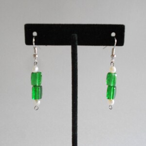 Pu&ograve; includere: Un paio di orecchini pendenti in argento con perline di vetro verde e dettagli di perle bianche.