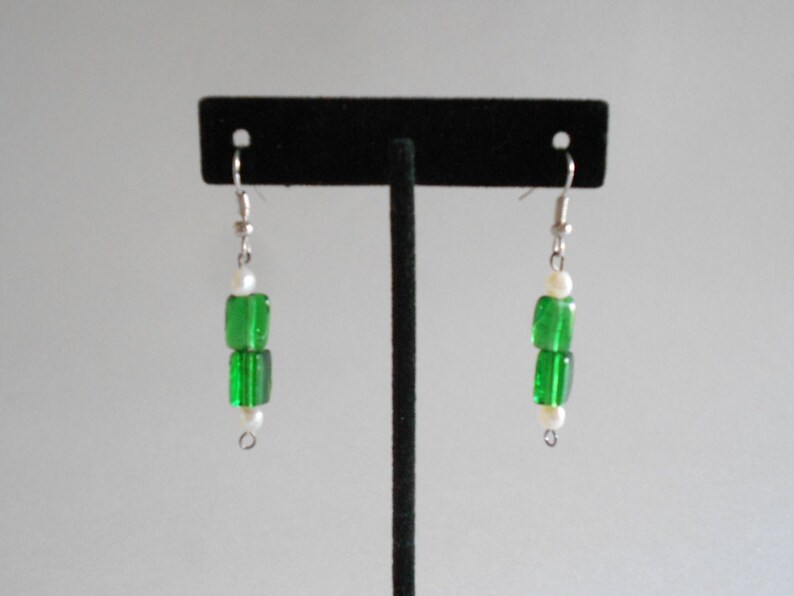 Pu&ograve; includere: Un paio di orecchini pendenti in argento con perline di vetro verde e dettagli di perle bianche.