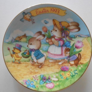 May include: A colorful ceramic plate with a gold rim features a scene of bunnies and a chick celebrating Easter. The plate has the text "Easter 1993" on it.
