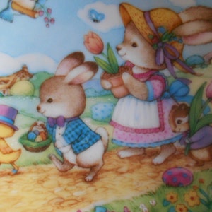 May include: A pastel-colored ceramic plate with a whimsical Easter scene. A yellow chick with a top hat holds a wand, while two bunnies, one wearing a straw hat and the other a blue plaid jacket, walk along a path. A brown squirrel carries a pink tulip.