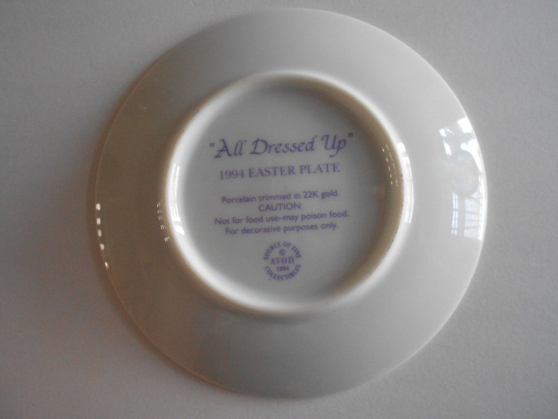 Pode incluir: Um prato de porcelana branco com uma inscri&ccedil;&atilde;o roxa que diz "All Dressed Up" 1994 Easter Plate. O prato &eacute; guarnecido com ouro de 22 quilates e &eacute; apenas para fins decorativos.