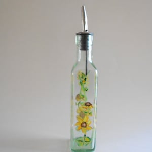 May include: A clear glass bottle with a silver pour spout and a painted design of yellow flowers and green leaves.