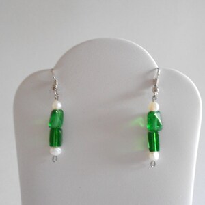 Pu&ograve; includere: Un paio di orecchini pendenti in argento con perline verdi e bianche. Gli orecchini hanno un design semplice e sono perfetti per l'uso quotidiano.