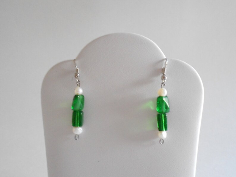 Pu&ograve; includere: Un paio di orecchini pendenti in argento con perline verdi e bianche. Gli orecchini hanno un design semplice e sono perfetti per l'uso quotidiano.