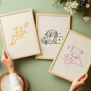 May include: Three light wood framed prints featuring minimalist line art illustrations of dogs. One print shows a yellow dog jumping for a disc, another a black dog at a laptop, and the third a pink dog interacting with a box marked with a question mark.