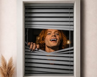 May include: A window with grey horizontal blinds partially opened to reveal a person with wavy ginger hair, sharp fangs, and long black fingernails peering through the slats. The person is positioned in the center of the window frame.