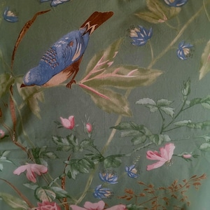 May include: A fabric with a botanical design featuring a blue bird perched on a branch. The fabric has a teal background with pink roses, blue flowers, and green leaves. The bird has blue feathers and a brown head.