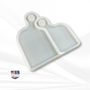 May include: White silicone mold for resin casting, featuring two rectangular shapes with rounded edges and a small circular indentation at the top of each shape.