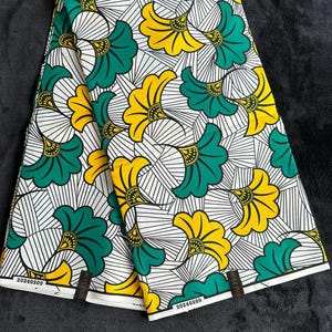 Puede incluir: Dos piezas de tela blanca con un patrón repetido de flores estilizadas verdes y amarillas. La tela tiene un patrón geométrico blanco y negro en el fondo. La tela tiene una etiqueta con el texto "20240209" y "WAX PRINT".