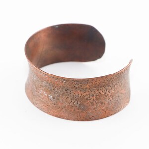May include: A wide copper bracelet with a hammered texture.