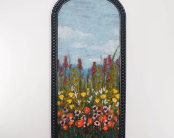 Pintura de paisaje en lana fieltrada con aguja, arte textil, maleza y flores silvestres a la luz del día.