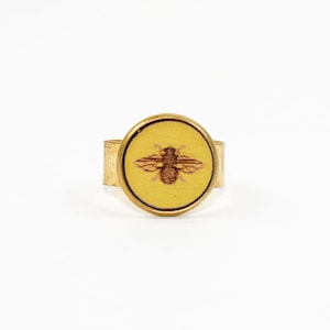 May include: A gold ring with a yellow round cameo featuring a brown bee design.