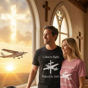May include: A man and woman wearing matching t-shirts with the text "Lifted in flight. Raised by faith." A small airplane flies in the background. The shirts are black and pink.