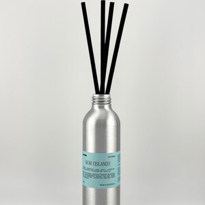 May include: A silver diffuser bottle with black reeds. The bottle has a light blue label with the text "KOH (ISLAND)" and other descriptive text. The diffuser is designed to release fragrance into the air.