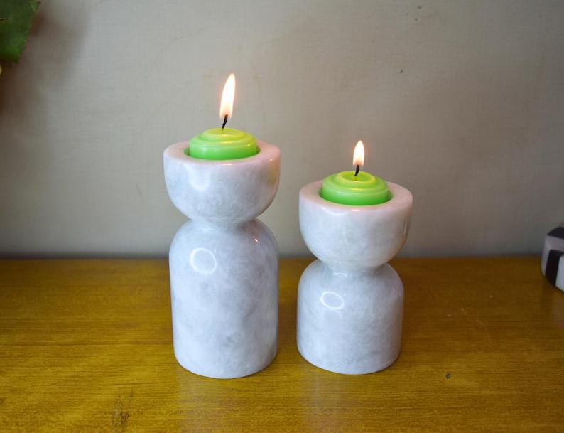 May include: Two white marble candle holders with green candles. The candle holders are hourglass shaped and have a smooth, polished finish.