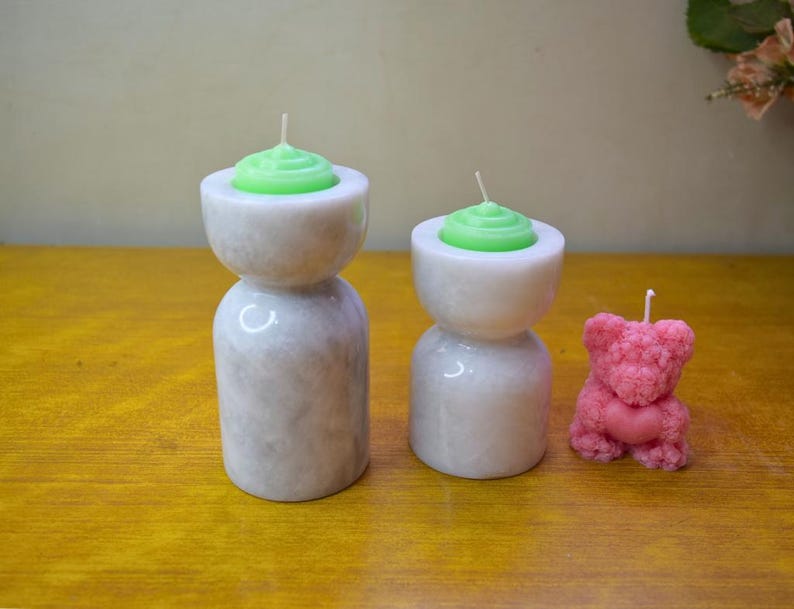 May include: Two white marble candle holders with green candles and a pink teddy bear candle.