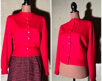 May include: A bright red cardigan sweater with a button-up front and long sleeves. The sweater is on a mannequin and is cropped at the waist.