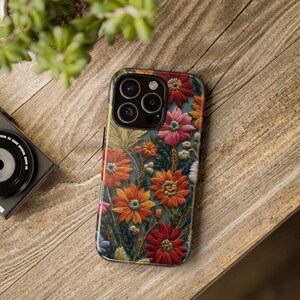 May include: A phone case with a floral design. The case is black and features a variety of colorful flowers, including red, orange, yellow, and pink. The flowers are embroidered on the case, giving it a textured look.