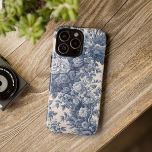 May include: A blue and white floral phone case with a camera lens cutout. The case has a vintage floral pattern.