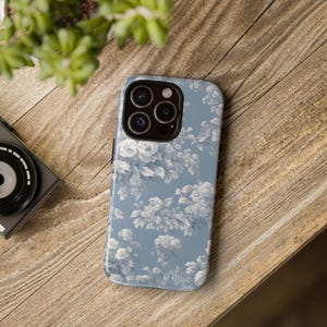 May include: A blue phone case with a white floral pattern. The case has a camera lens cutout and a raised lip around the edges.