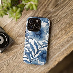 May include: A white phone case with a blue floral design. The case has a camera lens cutout and a white background.