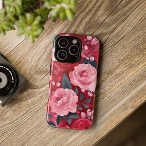 May include: A pink and red floral phone case with a camera lens cutout. The case has a detailed floral pattern with pink roses and green leaves.
