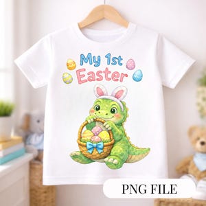 May include: White short-sleeved t-shirt featuring a green dinosaur wearing bunny ears and holding a basket of Easter eggs. The text "My 1st Easter" is above the dinosaur. The shirt is hanging on a wooden hanger.