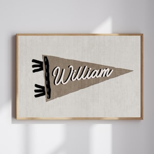 Puede incluir: Un banderín marrón con costuras negras y bordes deshilachados. El banderín tiene el nombre "William" escrito en letras blancas cursivas.