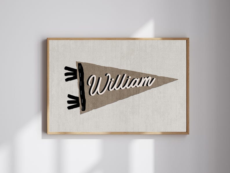 May include: A brown pennant banner with black stitching and frayed edges. The banner has the name "William" written in white cursive lettering.
