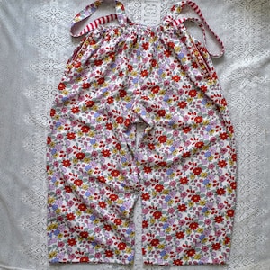 Op de afbeelding: Witte overall met bloemenprint en rode bandjes. De overall heeft een losse pasvorm en is gemaakt van een lichtgewicht stof.