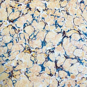 Pode incluir: Uma folha de papel com um padrão marmoreado de formas orgânicas rodopiantes em tons de creme, bege e amarelo claro, acentuadas por veios azul-profundo e castanho-escuro que criam uma rede complexa e interligada na superfície.