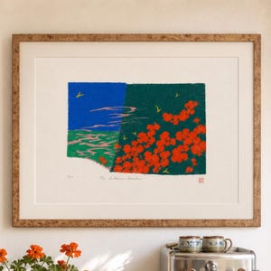 May include: A framed print featuring a stylized landscape with a blue sky, green hills, and red flowers, hanging above a stainless steel espresso machine, a potted geranium, and several ceramic mugs on a tiled counter with a green striped curtain.