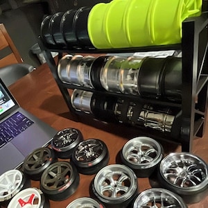 Może przedstawiać: Kolekcja srebrnych i czarnych kół z oponami, niektóre znajdują się na czarnym metalowym stojaku. Koła są ułożone na drewnianym stole. W tle znajdują się również żółte i zielone koła.