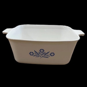 May include: A square white ceramic baking dish with integrated side handles. The exterior features a centered blue floral pattern consisting of three stylized flowers with pointed petals and thin leaves arranged in a symmetrical horizontal cluster.