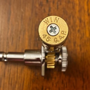 May include: A gold-colored guitar tuning peg with a brass casing that reads "WIN 45 G.A.R."