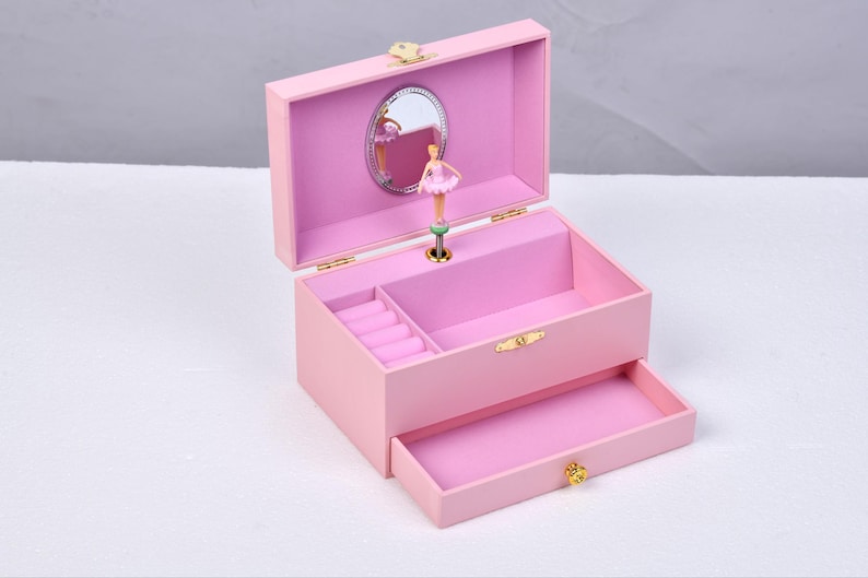 May include: A pink wooden ballerina music box with a mirror, a ballerina figurine, and a drawer. The music box has a ring holder inside.