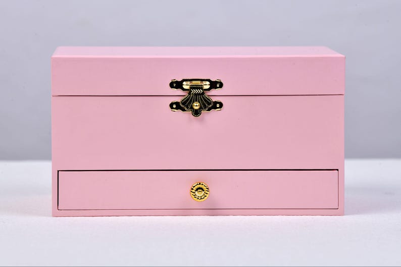 May include: A pink wooden jewelry box with a gold latch and a drawer with a gold knob.