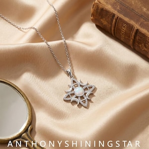 May include: A silver-toned necklace featuring a pendant with a central round iridescent opal stone, surrounded by four crescent moon shapes and small clear pavé crystals arranged in a star-like pattern, suspended from a delicate silver-toned chain.