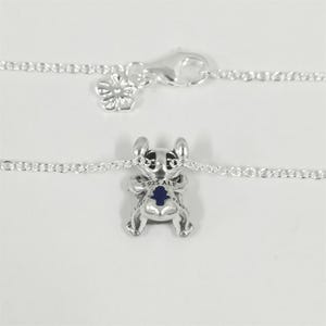 K&ouml;nnte beinhalten: Eine silberne Halskette mit einem Anh&auml;nger in Form einer Zeichentrickfigur. Der Anh&auml;nger hat eine blaue Mitte und ist mit "S925 ALE" gekennzeichnet. Die Kette und der Verschluss der Halskette sind ebenfalls silberfarben.