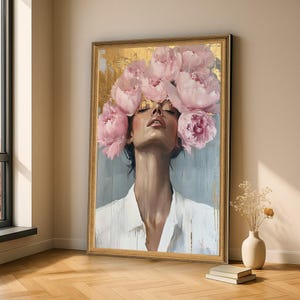 May include: A framed vertical wall art print depicting a person with eyes closed, wearing a white collared shirt, with a large arrangement of soft pink peony flowers surrounding the head against a textured gold and grey background.